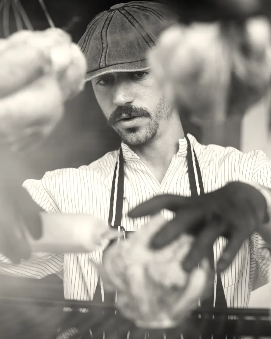 Octa at the grill in his cap, broccoli in his gloved hands, chickens hanging around him