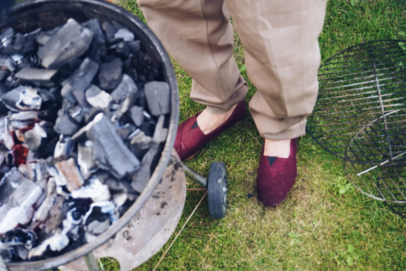 The round garden grill loaded with charcoal, the grate still on the grass