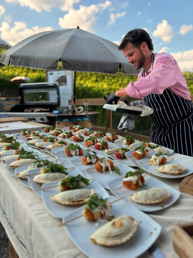 Plating one dish at a time along a long table under a parasol