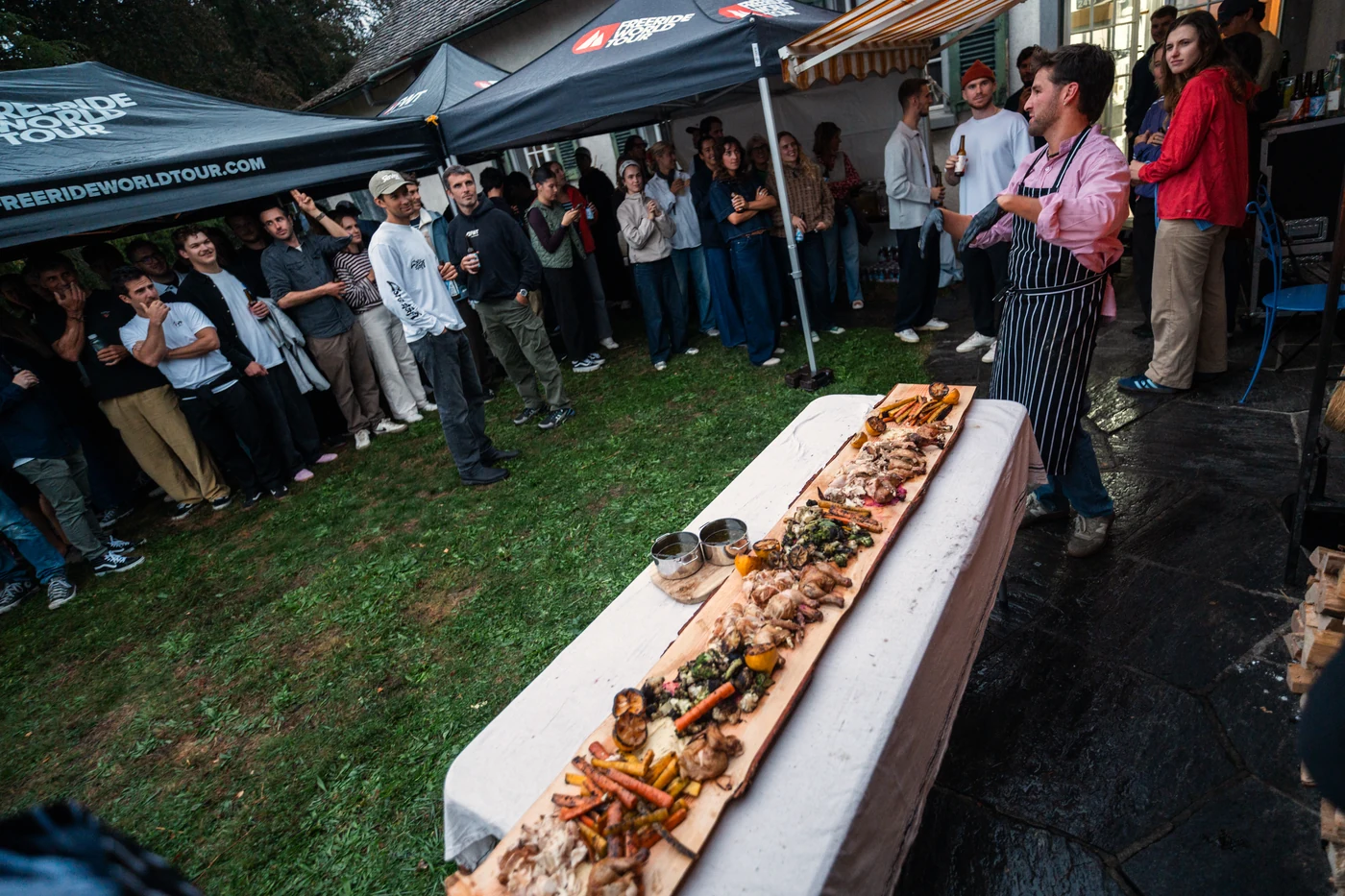 A long plank of chickens and roast vegetables down the table, the party standing around it