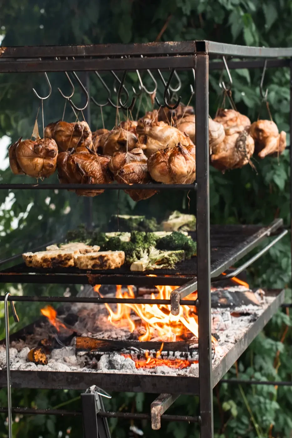 Chickens hanging on top, broccoli on the grill, the fire underneath