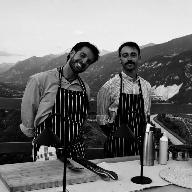 Two of the crew in aprons, the mountains behind them